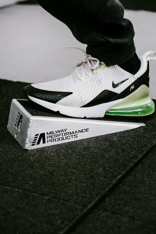 Akan Milway wearing white sneakers using the slant board to stretch ankles and calves with 'Milway Performance Products' branding visible.